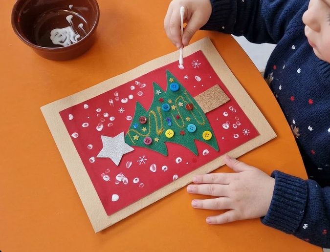 A child decorating a festive greeting card with a little fir tree